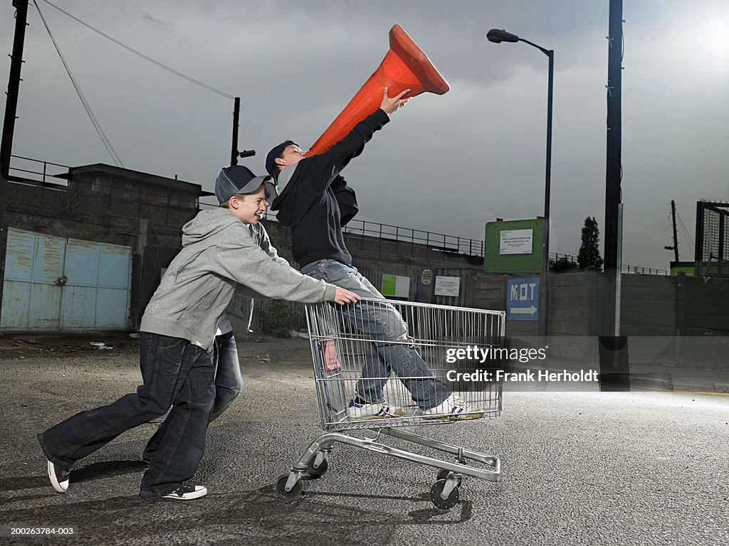 Teenage boys (13-15) pushing friend holding traffic cone in trolley
