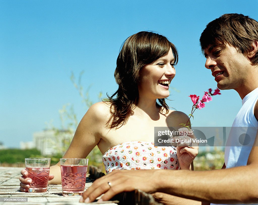 Couple having drinks on roof garden, woman holding flower, smiling