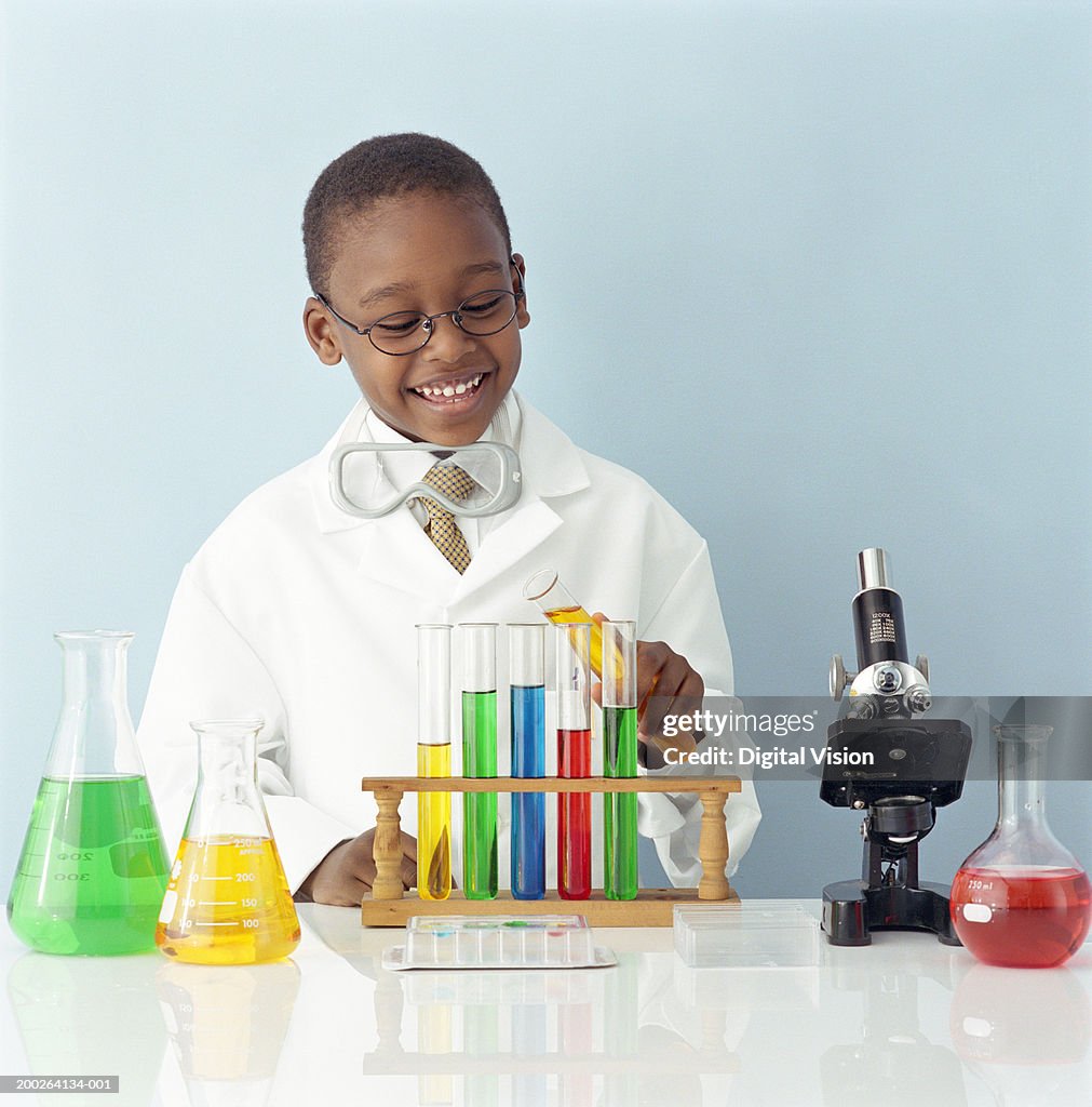 Boy (5-7) wearing white coat holding test tube in laboratory, smiling