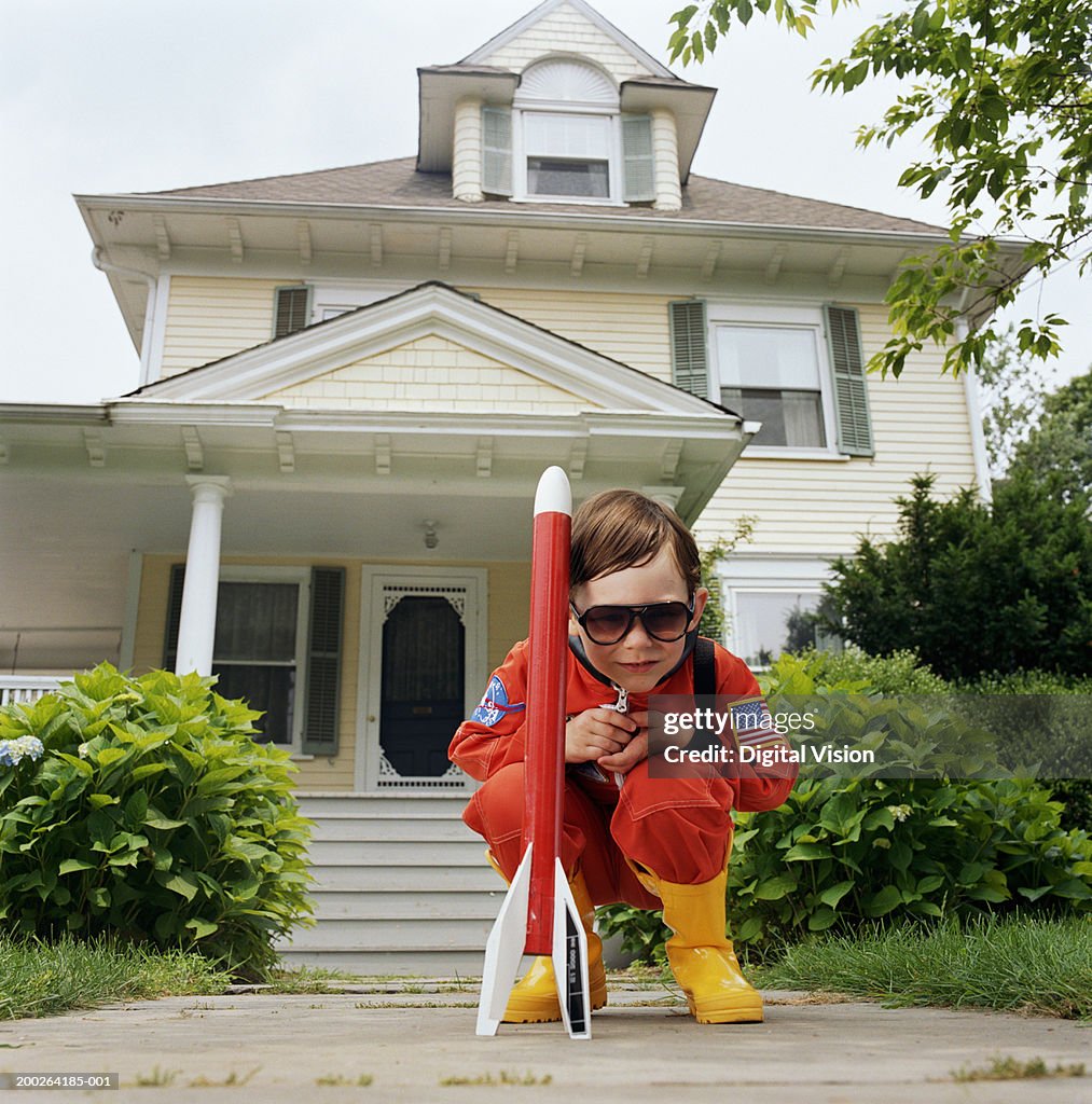 Boy (3-5) wearing sunglasses, crouching by toy rocket