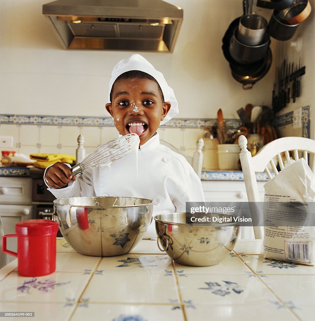 Boy (3-5) wearing chef outfit licking wisk, portrait