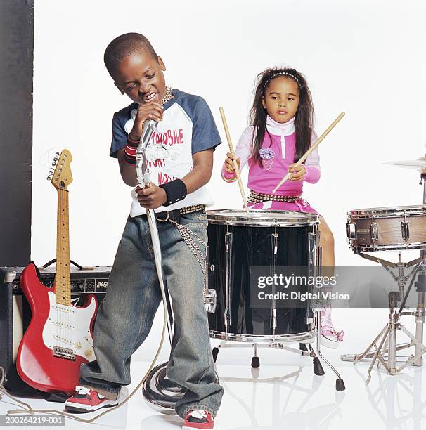 boy (9-11) singing into microphone by girl (7-9) playing drums - rock band white background stock pictures, royalty-free photos & images