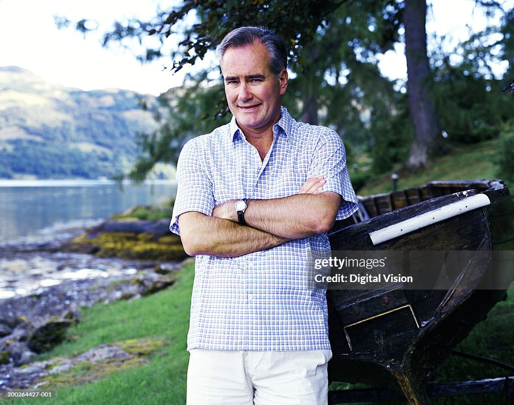 Man leaning on boat by river, arms crossed, smiling, portrait