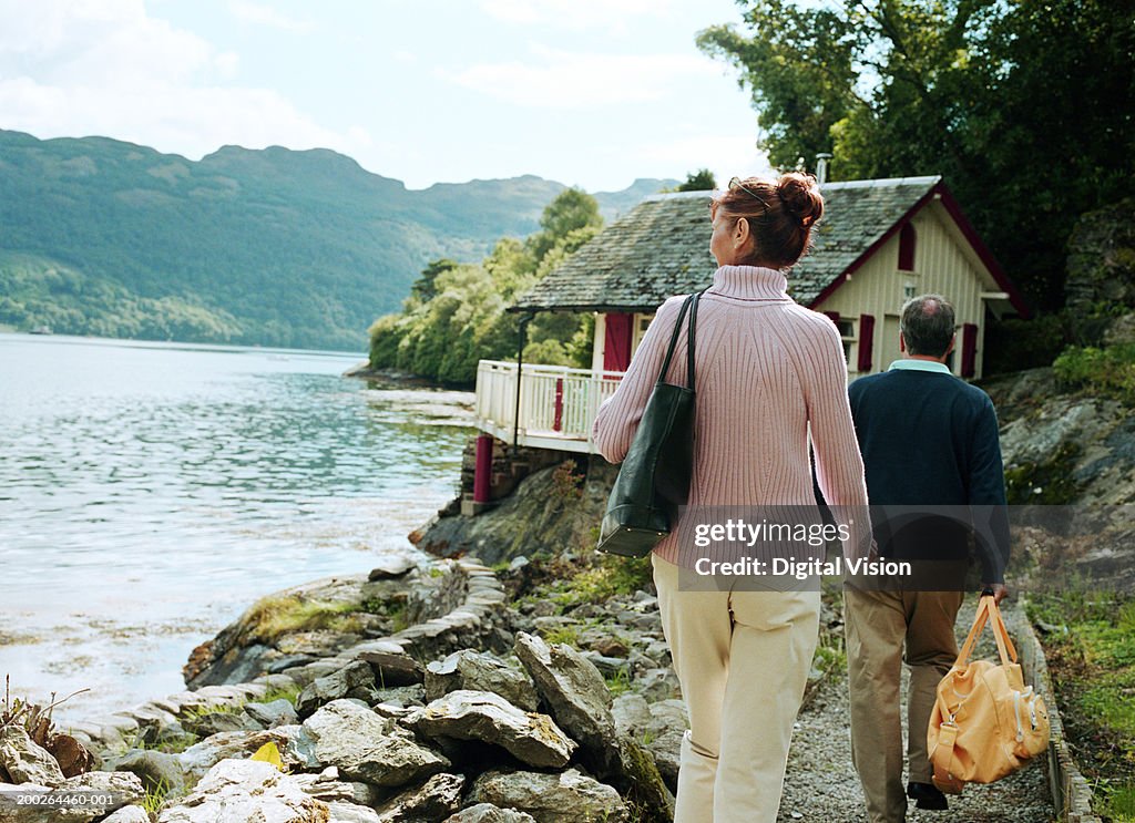 Couple walking towards house by water, rear view