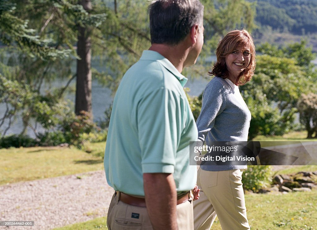 Couple walking outdoors holding hands, woman smiling at man