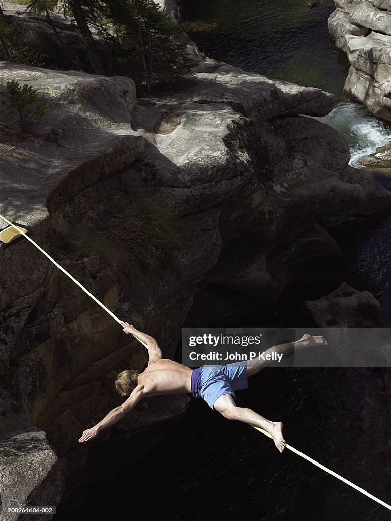 Young man balancing face down on slackline above canyon