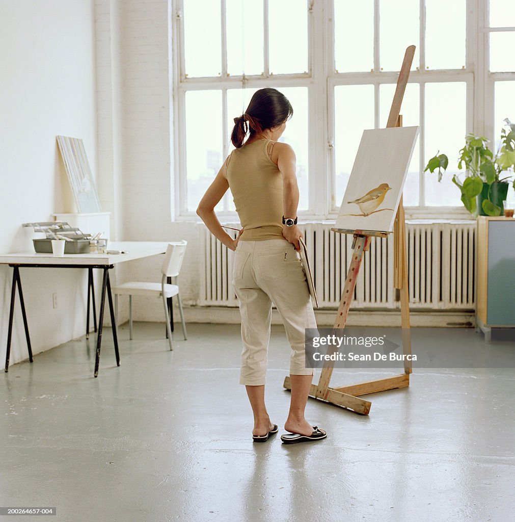 Female artist looking at painting on easel, rear view