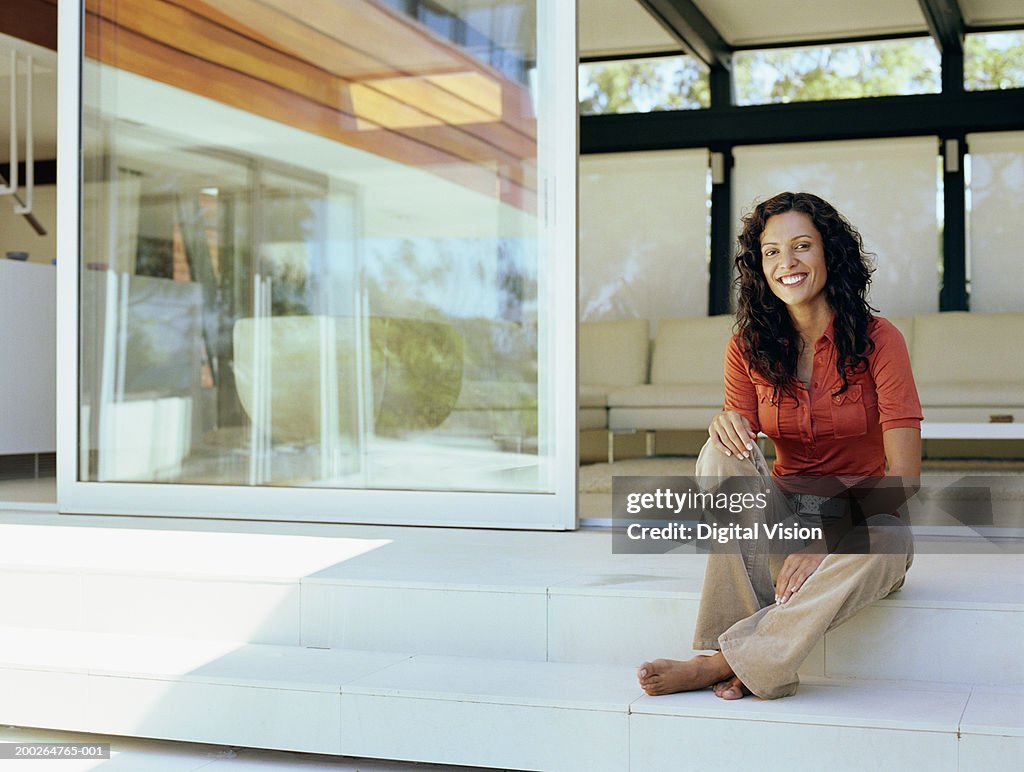 Woman sitting on steps by house, smiling, portrait