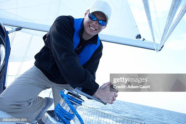 man wearing sunglasses turning winch handle on yacht, smiling - flytväst bildbanksfoton och bilder