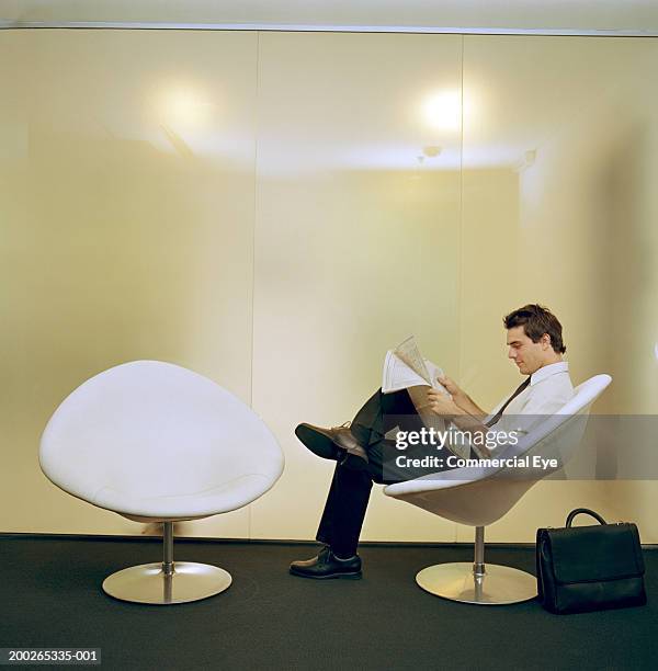 businessman sitting on chair, reading newspaper, side view - egg chair stockfoto's en -beelden