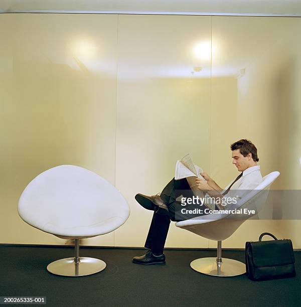 businessman sitting on chair, reading newspaper, side view - ball chair stock pictures, royalty-free photos & images