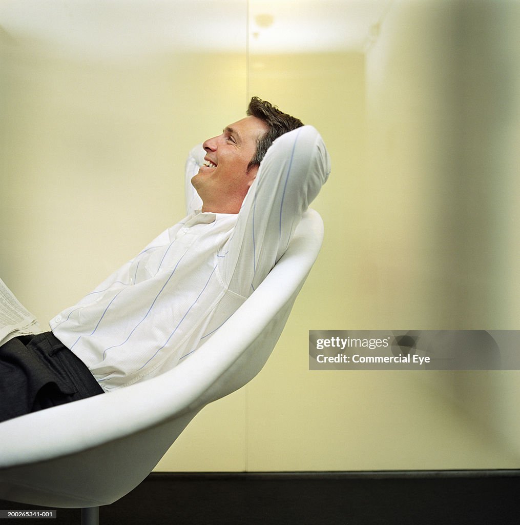 Man relaxing on chair, arms behind head, side view