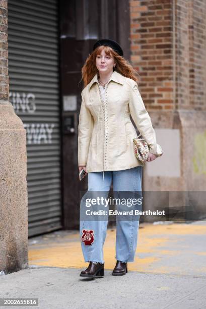 Guest wears a black beret hat, a beige gathered corset lace-up jacket , a floral print bag, ripped blue denim jeans pants with a red patch "Girls...