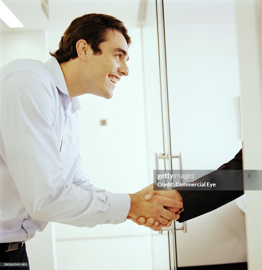 Man shaking hands with colleague behind cubicle, side view