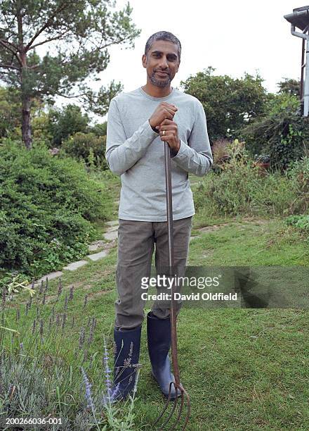 mature man standing with garden fork on grass, portrait - fourche photos et images de collection