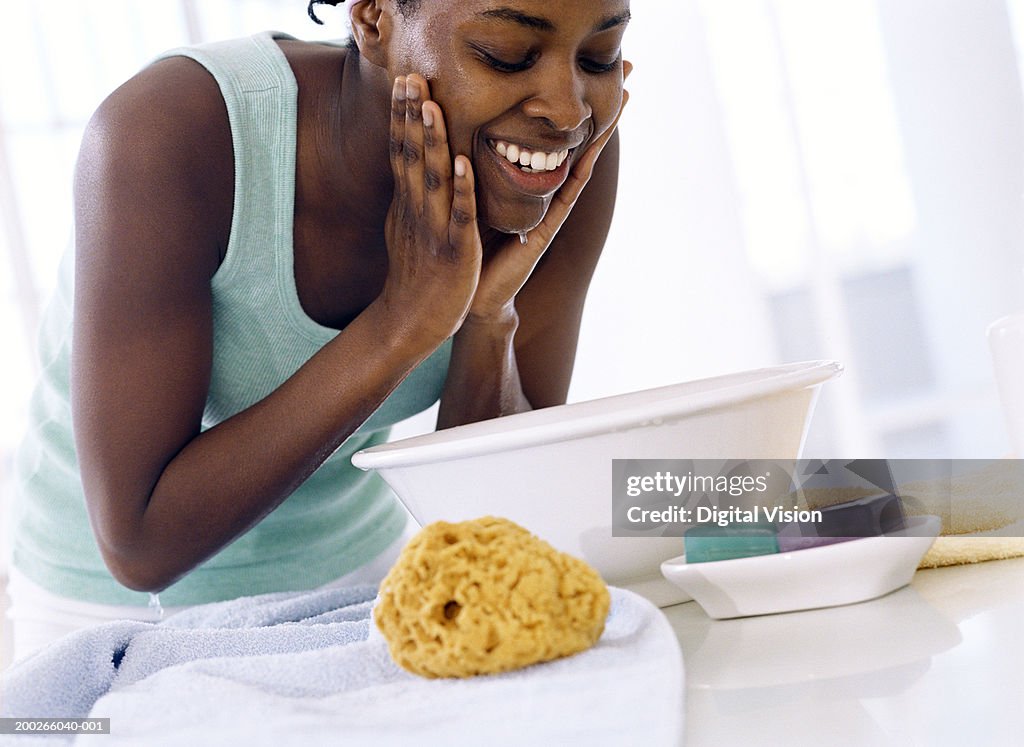 Young woman bent over bowl, washing face, smiling