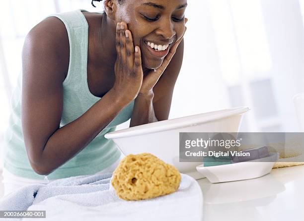 young woman bent over bowl, washing face, smiling - woman face cleaning stock pictures, royalty-free photos & images