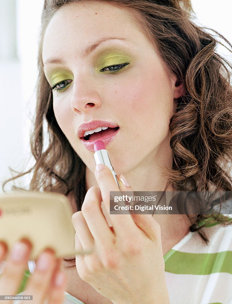 Young woman applying lipstick in compact mirror, close-up