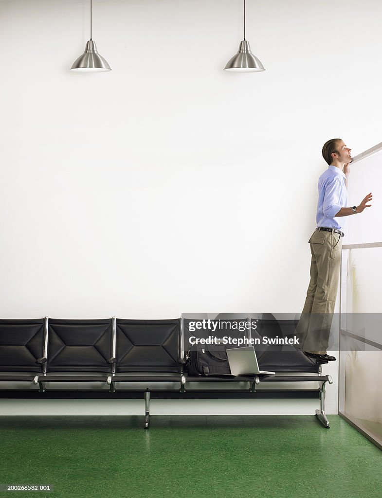 Businessman standing on chair, looking over waiting room divider