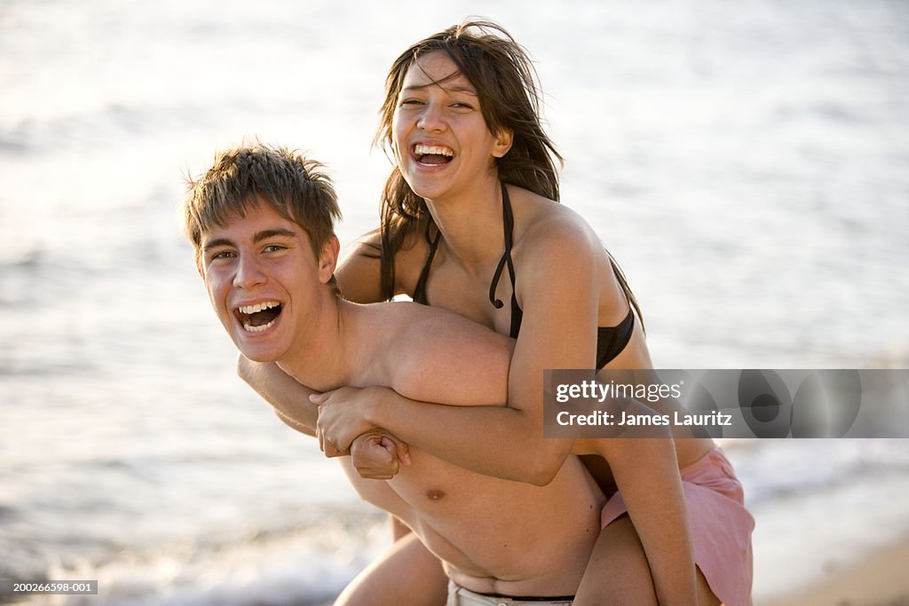 Teenage couple (15-17) laughing, boy giving girl piggyback, portrait