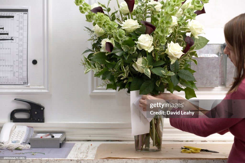 Female florist securing card to bouquet of flowers in vase, side view