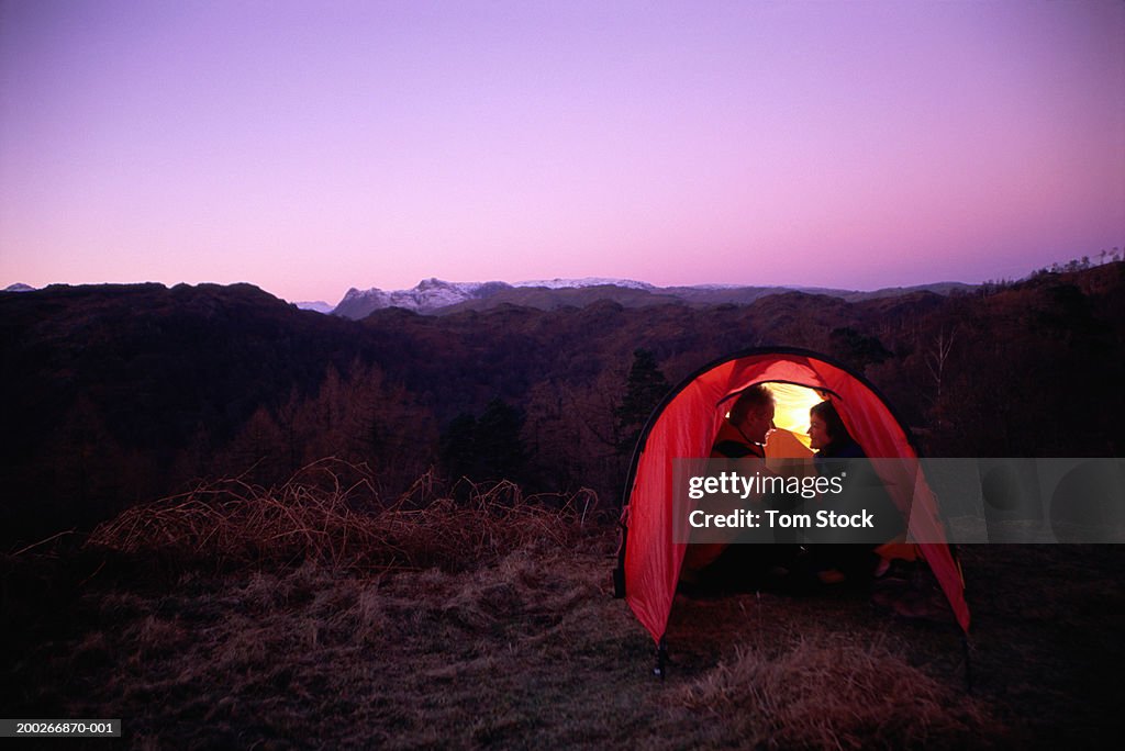 Couple sitting in tent overlooking countryside, dusk