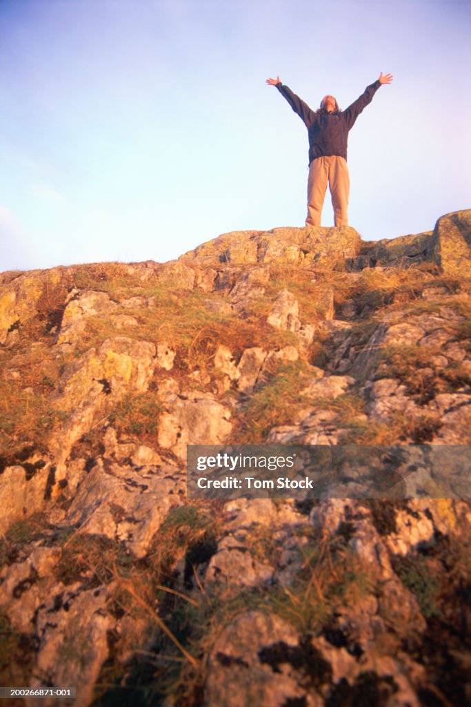 Female hiker standing on hill, arms outstretched, low angle view