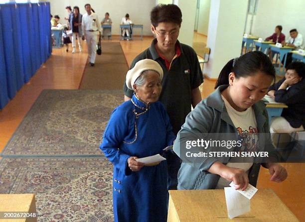 An old woman, accompanied by her son and dressed in traditional Mongolian garb, waits to vote behind a teenager at a balloting office 02 July 2000 in...