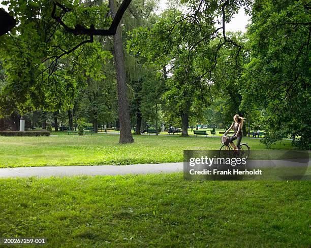 young woman riding bicycle on path through park - adult riding bike through park stock pictures, royalty-free photos & images