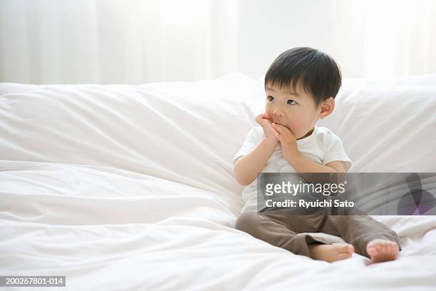 baby boy (18-21 months) sitting on bed sucking thumb - chuparse el pulgar fotografías e imágenes de stock