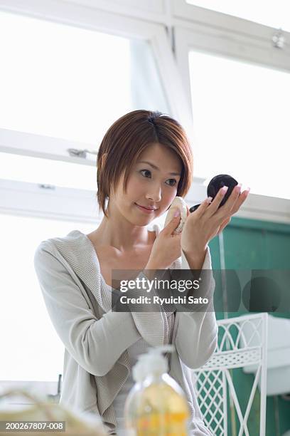 young woman applying make-up in compact mirror, smiling - powder puff stock pictures, royalty-free photos & images