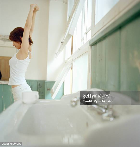 young woman stretching in bathroom, arms raised, profile - bathroom exercise stock pictures, royalty-free photos & images