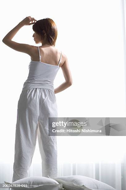 young woman standing by window, hand to head, rear view - cami stock-fotos und bilder