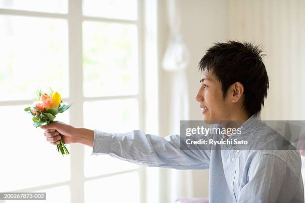 young man holding out bunch of flowers, smiling, profile - man holding out flowers stock pictures, royalty-free photos & images