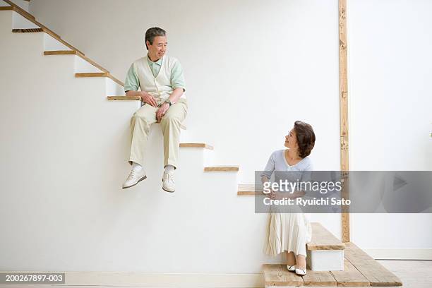 mature couple sitting on stairs at different heights, looking at one another - japanese tree stockfoto's en -beelden