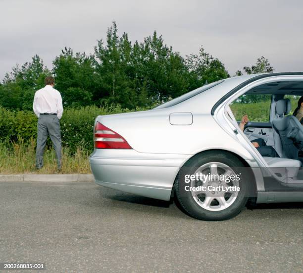 businessman urinating at side of road by car, rear view - peeing men fotografías e imágenes de stock