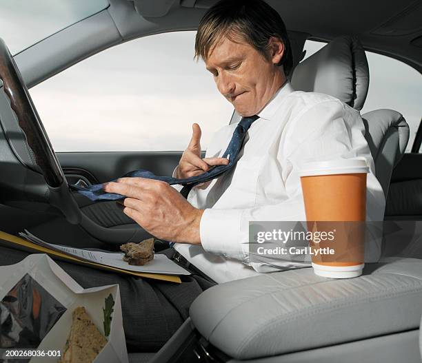 mature businessman having lunch in car, wiping tie with finger - 40's rumpled business man stockfoto's en -beelden