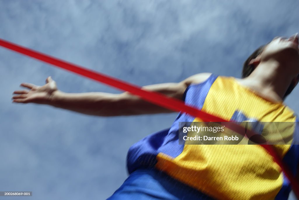 Male runner breaking tape, crossing finish line (blurred motion)