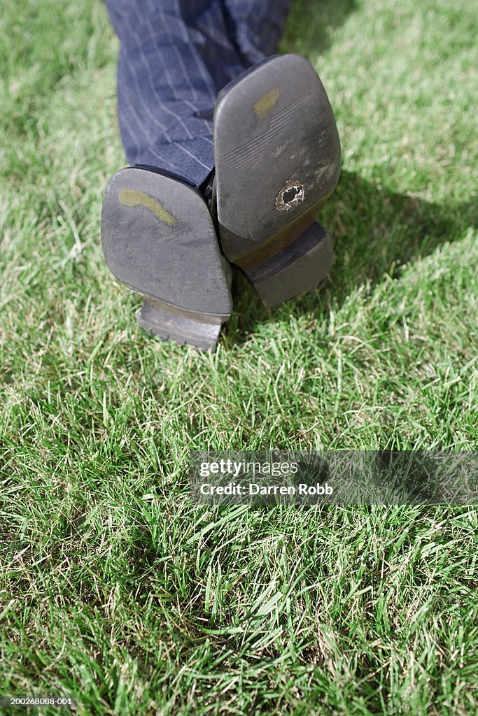 Man lying on grass, holes in his shoes, low section