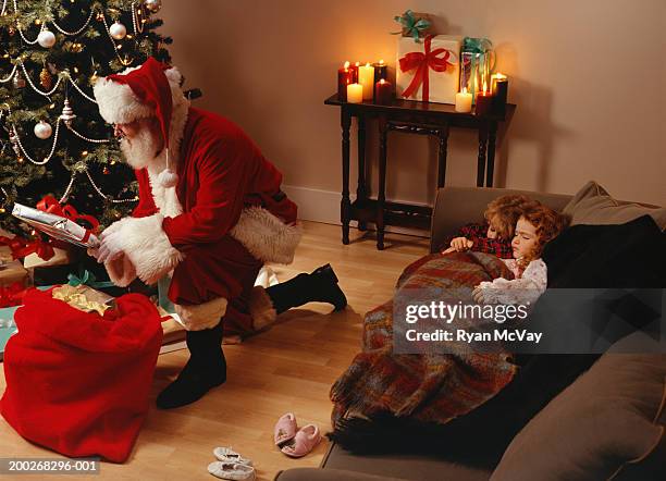 santa claus putting presents under christmas tree - nikolausstiefel stock-fotos und bilder