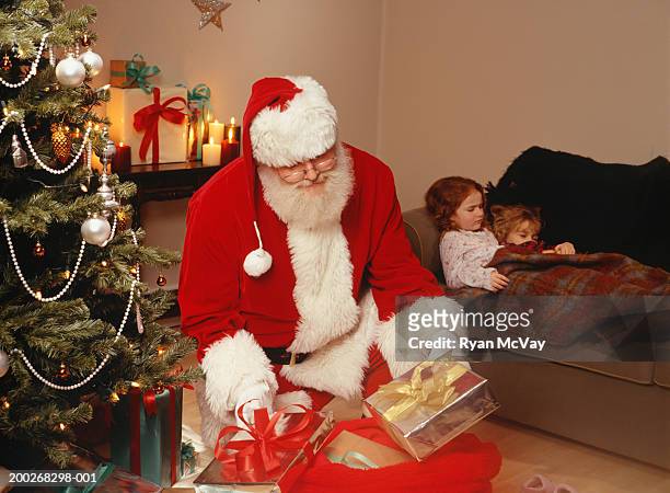 santa claus putting presents under christmas tree - nikolausstiefel stock-fotos und bilder