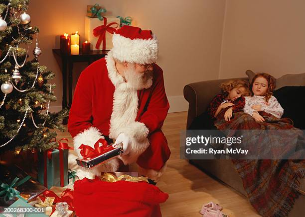 santa claus putting presents under christmas tree - nikolausstiefel stock-fotos und bilder