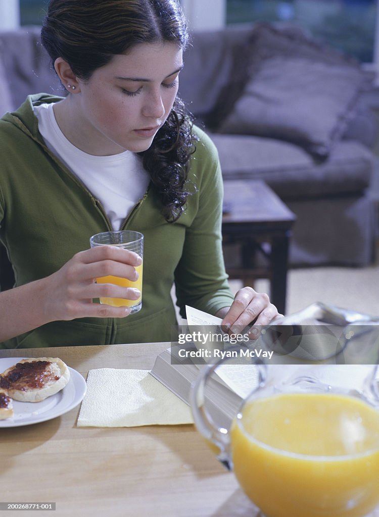 Teenage girl (16-17) reading book at breakfast table