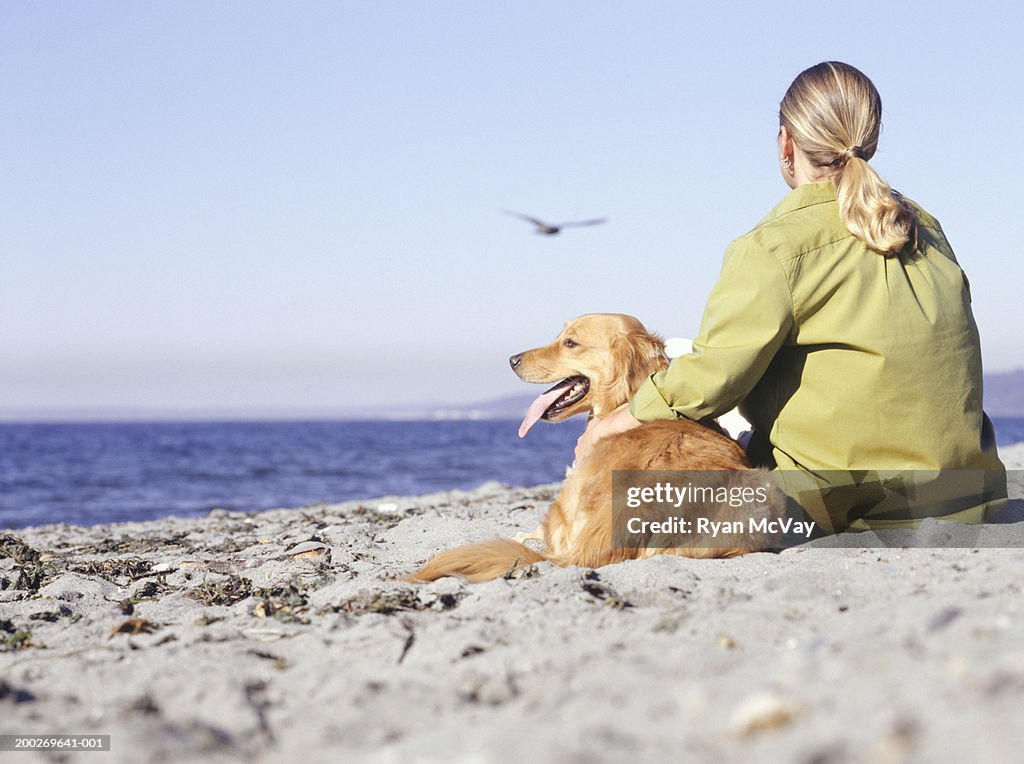 Young woman sitting with Golden Retriever on beach