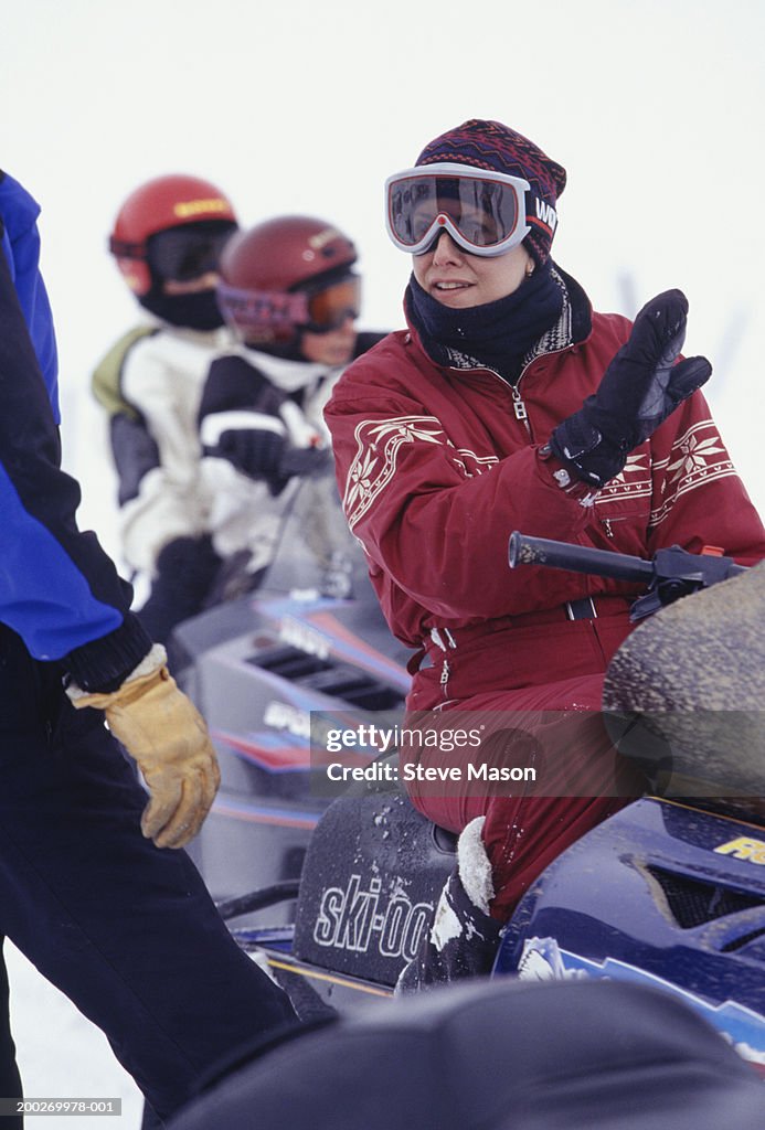 People with snowmobiles talking on slope, two children in background