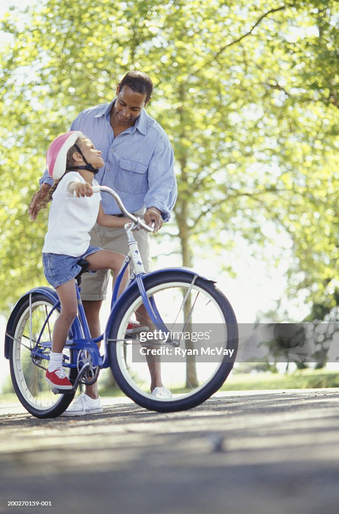 Father teaching daughter (4-5) to ride bicycle in park