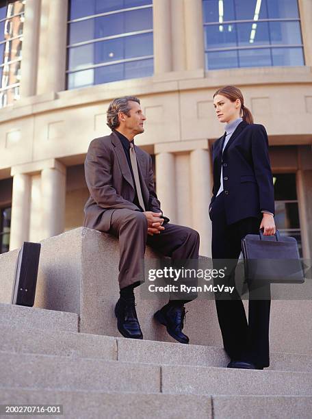 two businesspeople talking outside large building, low angle view - low angle view of two businessmen standing face to face outdoors stock pictures, royalty-free photos & images