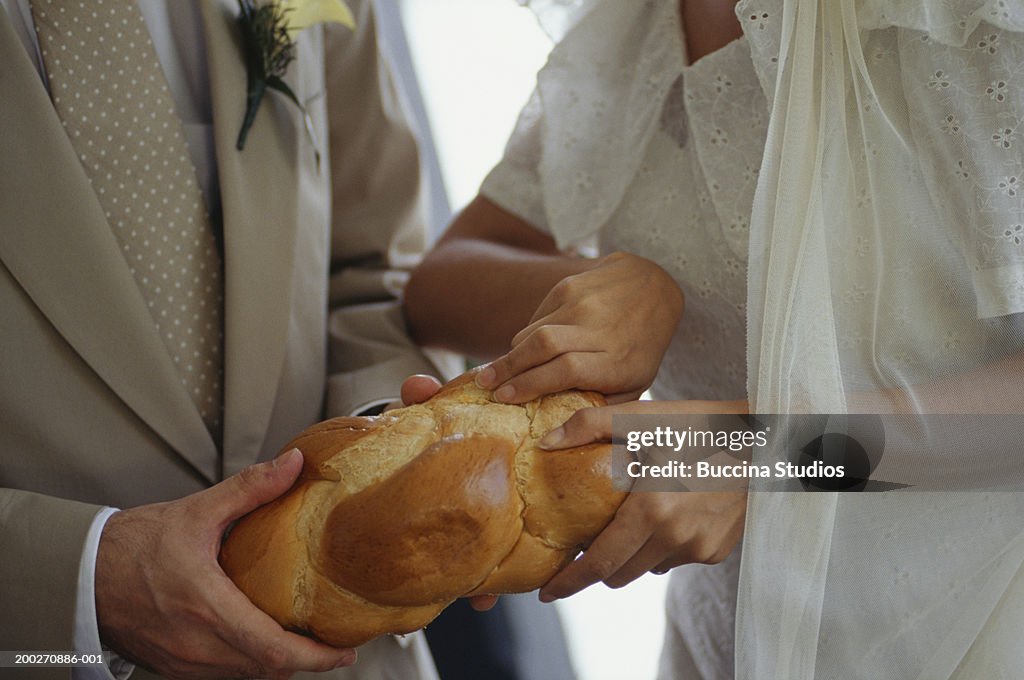Bride and groom breaking challah, close-up of hands
