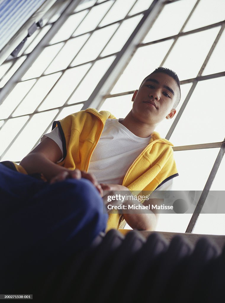 Teenage boy (16-17) sitting indoors beside window, low angle view