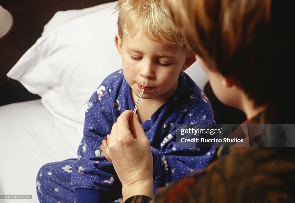 Mother taking sons (3-4) temperature in bedroom, close-up